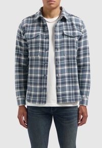 Blauw-wit geruite shirt van zachte stof, met twee borstzakken, knopen aan de voorkant en lange mouwen, gelaagd over een wit T-shirt.