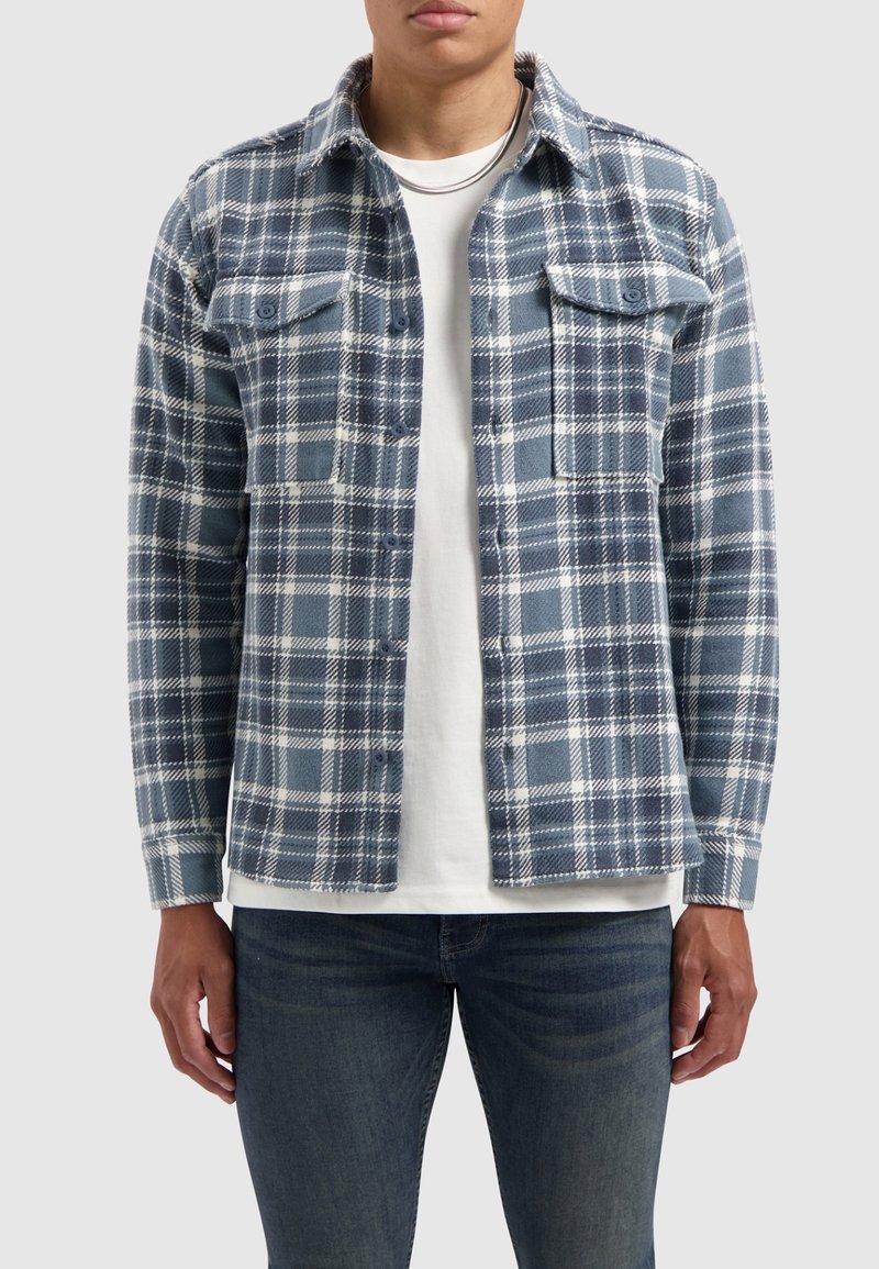 Blauw-wit geruite shirt van zachte stof, met twee borstzakken, knopen aan de voorkant en lange mouwen, gelaagd over een wit T-shirt.