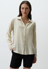 Crème overhemd met subtiel bloemenpatroon, lange mouwen en een kraag. Gepaard met zwarte shorts, minimalistisch ontwerp.