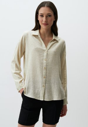 Crème overhemd met subtiel bloemenpatroon, lange mouwen en een kraag. Gepaard met zwarte shorts, minimalistisch ontwerp.
