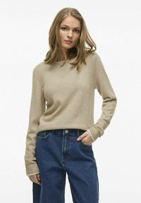 Suéter beige de punto con mangas largas, puños acanalados y cuello redondo, combinado con jeans de mezclilla azul de talle alto.