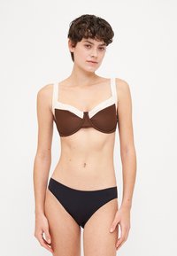 Barna és krémszínű, két tónusú bikini felső széles pántokkal, alátámasztó merevítőkkel és sima textúrával, valamint illő fekete bikini alsóval.