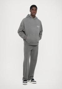 Gray hoodie with a front pocket and printed logo, paired with matching gray pants. Outfit features a relaxed fit and soft texture.