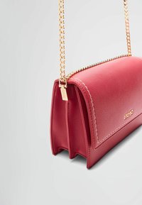 Bolso de mano de cuero rojo con una forma estructurada, cadena para el hombro y herrajes dorados. Presenta un contorno cosido y un detalle del logo.