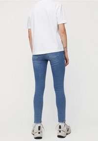 Camiseta blanca de manga corta, jeans ajustados azules y zapatillas grises. Tejido suave, ajuste casual y diseño minimalista sin patrones visibles.