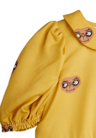 Kollane pikapoole varrukatega rõivas, millel on pugevate varrukatega ja tumeda ja heleda pruuni värvi koomiksite ahvi näod kangal. Krae on lapik ja terav.