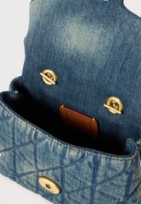 Ανοιχτό τσόχα τζιν πορτοφόλι που δείχνει κλειδώματα με χρυσή επίστρωση και μια μικρή καφέ δερμάτινη ετικέτα στο εσωτερικό.