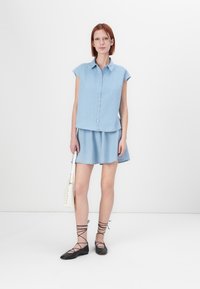 Light blue denim shirt with short sleeves, buttoned front, and matching denim skirt. Black lace-up flats and a white handbag complete the look.