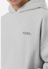 Lichtgrijze fleece hoodie met een zachte textuur, voorzien van een voorzak en een klein, geborduurd logo op de borst.