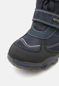Must ja tumesinised matkasaapad, millel on tekstuuriga võrgukangas, kummist tald ja Velcro rihm. Omab siniseid õmblusi ja kihilisi disainielemente.