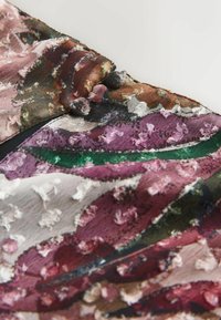 Gros plan d'un tissu texturé avec des motifs floraux multicolores en relief dans les tons de rose, vert et marron, ornés de petits boutons recouverts de tissu.