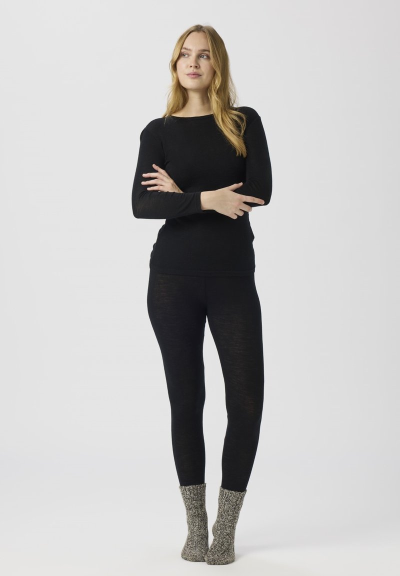 Svart langermet topp kombinert med svarte leggings og grå strikkede sokker. Antrekket har en tettsittende design og myk tekstur.