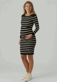 Svart- och vitrandig amningsklänning med långa ärmar och figurnära Silhuett, tillverkad av mjukt tyg. Matchad med ljusa sneakers.