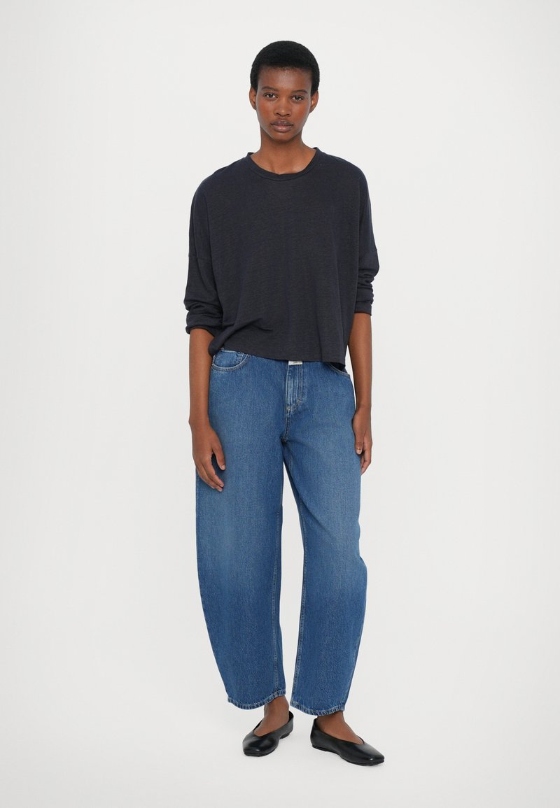 Marineblaues Langarmshirt mit lockerer Passform, kombiniert mit hellblauen weiten Jeans und schwarzen flachen Schuhen. Einfaches Design mit entspannter Silhouette.