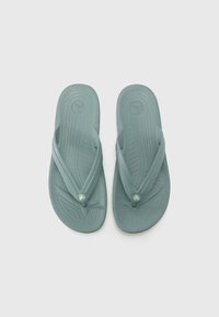 Mintin vihreät flip-flopit, jotka on valmistettu kumista ja joissa on tekstuuripohjat. Niissä on thong-nauharemmi ja pieni pyöreä logo keskellä.