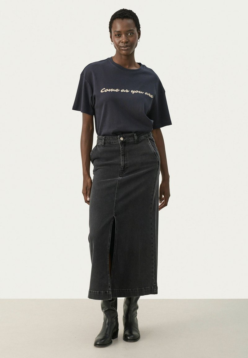 Navy t-shirt z napisem "Przyjdź takim, jaki jesteś", zestawiony z czarną spódnicą z dżinsu o wysokim stanie, z wyswobodzeniem z przodu. Model nosi czarne buty.