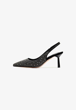 Pompe slingback en suède noir avec un bout pointu, ornée de clous métalliques et d'un talon aiguille noir brillant. Doublure intérieure lisse.