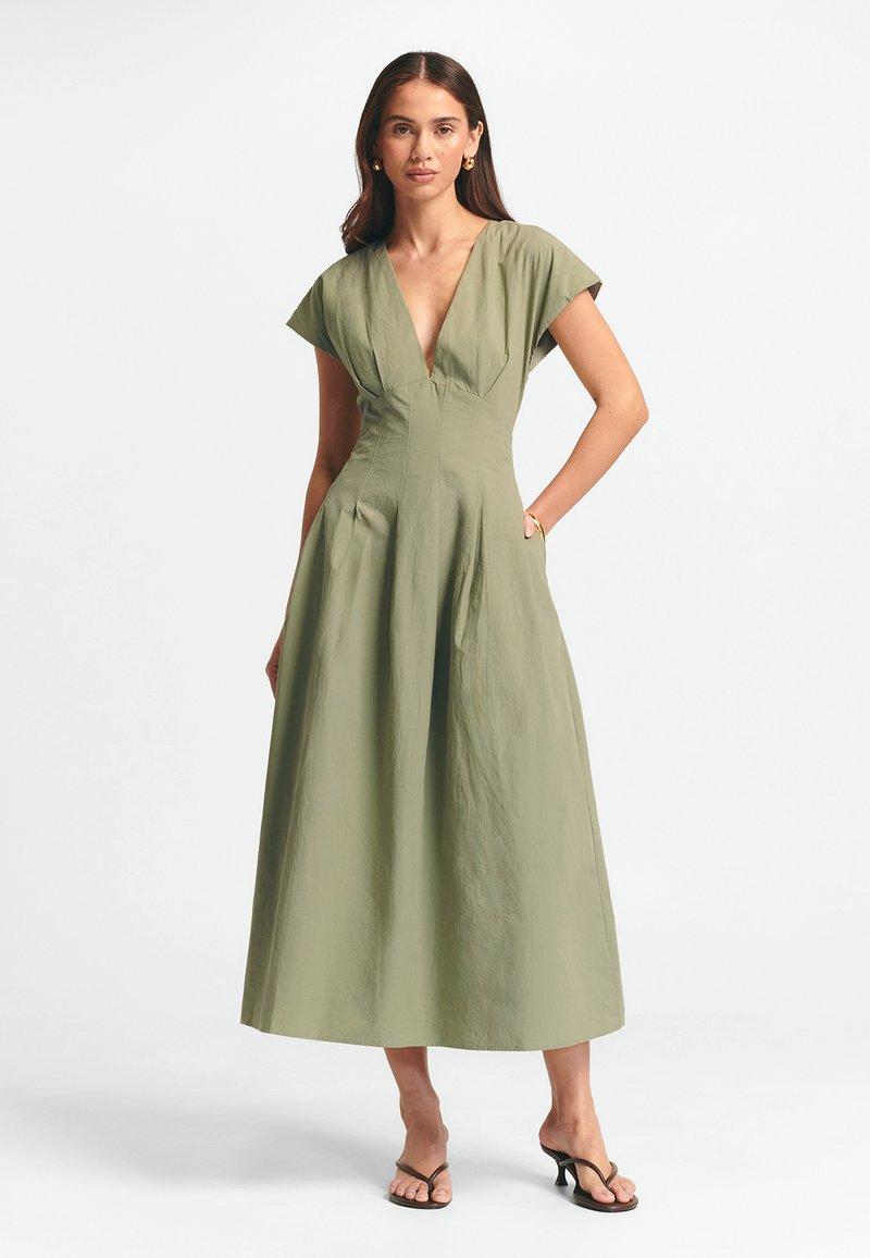 Vihreä oliivinvärinen hihaton maksimekko, jossa on syvä V-pääntie, laskostettu yläosa ja sivutaskut. Kangas on pehmeä ja teksturoitu.