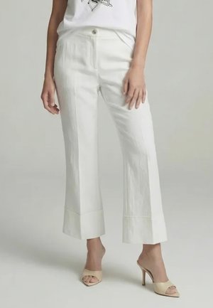 Woman wearing cropped wide-leg white pants paired with beige high-heeled open-toe mules and a partially visible white top.