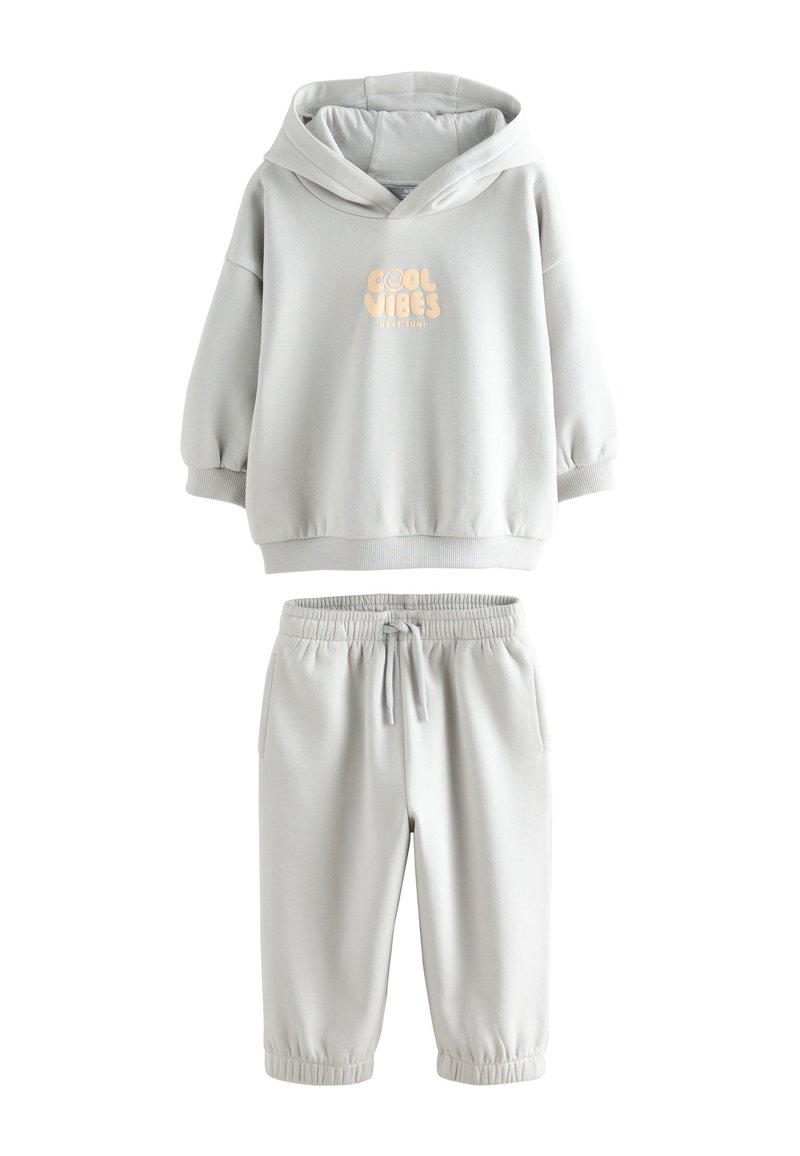 Hall halliga kapuutsiga dressipluus "COOL VIBES" trükiga ja hallide elastse vöökohaga spordipükstega. Pehme, sile kangas; lõdvestunud istuvus; soonikkoes mansetid.