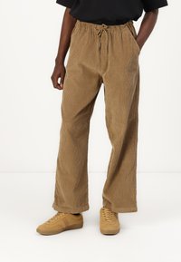 Brune corduroy bukser med en afslappet pasform, elastisk talje og snor. Kombineret med lysebrune sneakers. Tekstureret, lodret ribbet mønster.