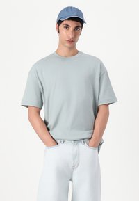 T-shirt en coton oversized bleu clair avec des manches courtes. Assorti avec un pantalon en denim délavé. La casquette présente une teinte bleue assortie et une visière courbée.