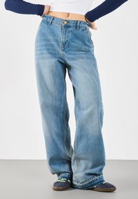 Lys blå denim vide ben jeans med høy midje, med knappelukking foran og falmet tekstur. Båret med mørke sneakers.