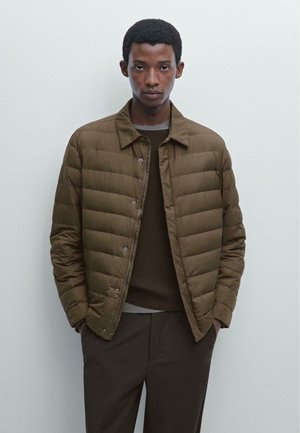 Brown puffer jacket with horizontal quilting, button front, and collared neck; worn over a dark sweater and matching trousers.