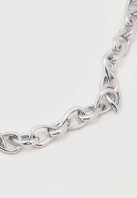 Κοντινό πλάνο ενός ασημένιου κολιέ αλυσίδας με διασυνδεδεμένους, επιμηκυμένους οβάλ κρίκους σε λευκό φόντο.