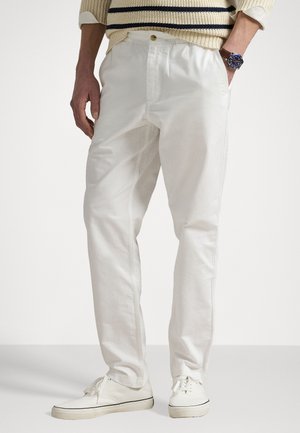 Calças de algodão brancas com um corte reto, apresentando um fecho de botão e bolsos laterais, combinadas com sapatilhas brancas. Design clássico, textura suave.