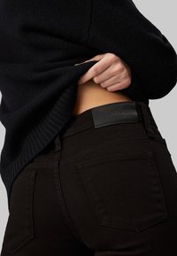 Svarta denimjeans med en slät textur och bakfickor, i kombination med en mörkstickad tröja. Fickor i läder vid midjan.