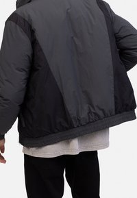 Black, puffer jacket with a matte finish, features a zippered front, elastic cuffs, and a cinched hem. Includes contrasting textured panels.