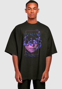 Sort oversized t-shirt med et grafisk design med lilla blomster og en ansigtssilhuet. Teksten lyder "SYNTHESIS" og "EVANESCENCE."