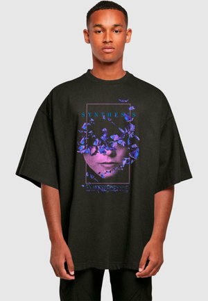 Svart overdimensjonert T-skjorte med et grafisk design med lilla blomster og en ansiktskontur. Teksten sier "SYNTHESIS" og "EVANESCENCE."