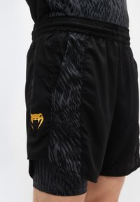 Μαύρο αθλητικό σορτς με υφασμάτινη μαύρη πλευρική ταινία με διακριτικό μοτίβο και χρυσό λογότυπο στο αριστερό πόδι. Περιλαμβάνει ελαστική μέση.