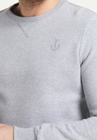 Sudadera gris hecha de una suave mezcla de algodón, que presenta un clásico cuello redondo y puños de canalé, con un sutil logo de ancla bordado en el pecho.