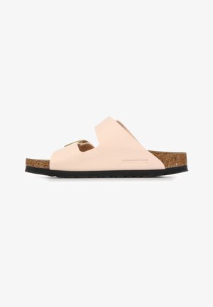Licht beige Birkenstock slippers met twee brede bandjes, kurken voetbed en zwarte rubberen zool, van opzij getoond.