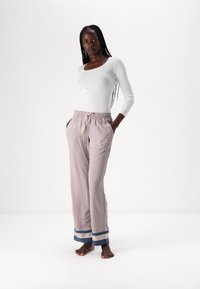 Witte lange mouwtop gecombineerd met licht gestreepte broek met blauwe en crèmekleurige boorden, een elastische tailleband en een trekkoord.