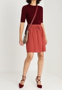 Maglione corto bordeaux a maniche corte abbinato a una gonna ruggine lunga fino al ginocchio, con vita elastica e cordino. Indossato con sandali rossi con fasce.