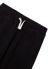 Czarne dresy z elastycznym paskiem i białym sznurkiem do regulacji. Posiadają boczne kieszenie i miękką, gładką teksturę.