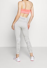 Leggings gris clair avec un motif camouflage sur le bas des jambes, associés à un soutien-gorge de sport rose avec un logo et des fines bretelles.