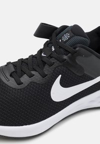 Scarpa sportiva nera con tomaia in mesh e sintetico, dotata di una bianca swoosh Nike, lacci neri piatti e una tabella posteriore strutturata nera.