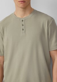 Lichtgrijs geribbeld shirt met korte mouwen en een ronde hals, voorzien van een knoopsluiting met drie knopen en een zachte textuur. Casual ontwerp, aansluitend gesneden.