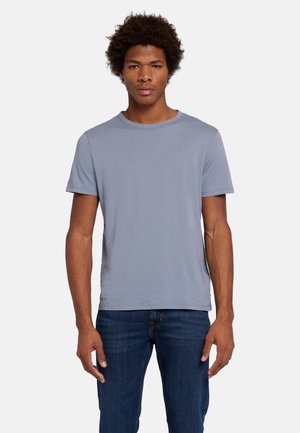 Lichtblauwe t-shirt met korte mouwen van een zachte stof met een ronde hals, gedragen met donkerblauwe spijkerbroek, staande tegen een effen achtergrond.
