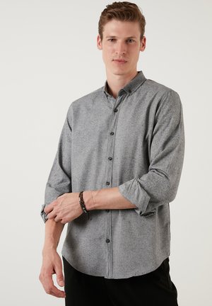 Camisa gris con botones, de tejido texturizado, mangas largas remangadas hasta los codos y botones oscuros. Dobladillo redondeado y detalle en el cuello.