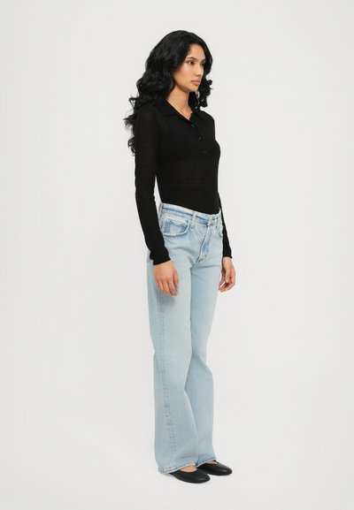 Black long-sleeve top with a collar and buttons, paired with light blue flared jeans. Model stands in profile against a plain background.