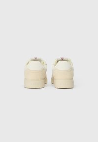 Tenisi cu un superior crem, accente din suede în nuanță de bej și vârf rotunjit. Prezintă un design distinctiv pe spate, cu un accent roz.