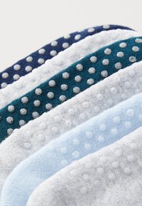 Fem par med sokker i mørkeblå, teal, hvit, lyseblå og grå, hver med teksturerte gummidots på sålene for bedre grep.