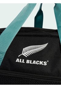 Sorte tote taske med teal stropper, der har et hvidt bregne-logo og teksten "ALL BLACKS". Lavet af slidstærkt stof med mesh-detaljer.