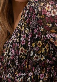 Robe noire à fleurs présentant un mélange de petites fleurs roses, jaunes et blanches. Tissu léger et transparent avec un design froncé et une texture douce.